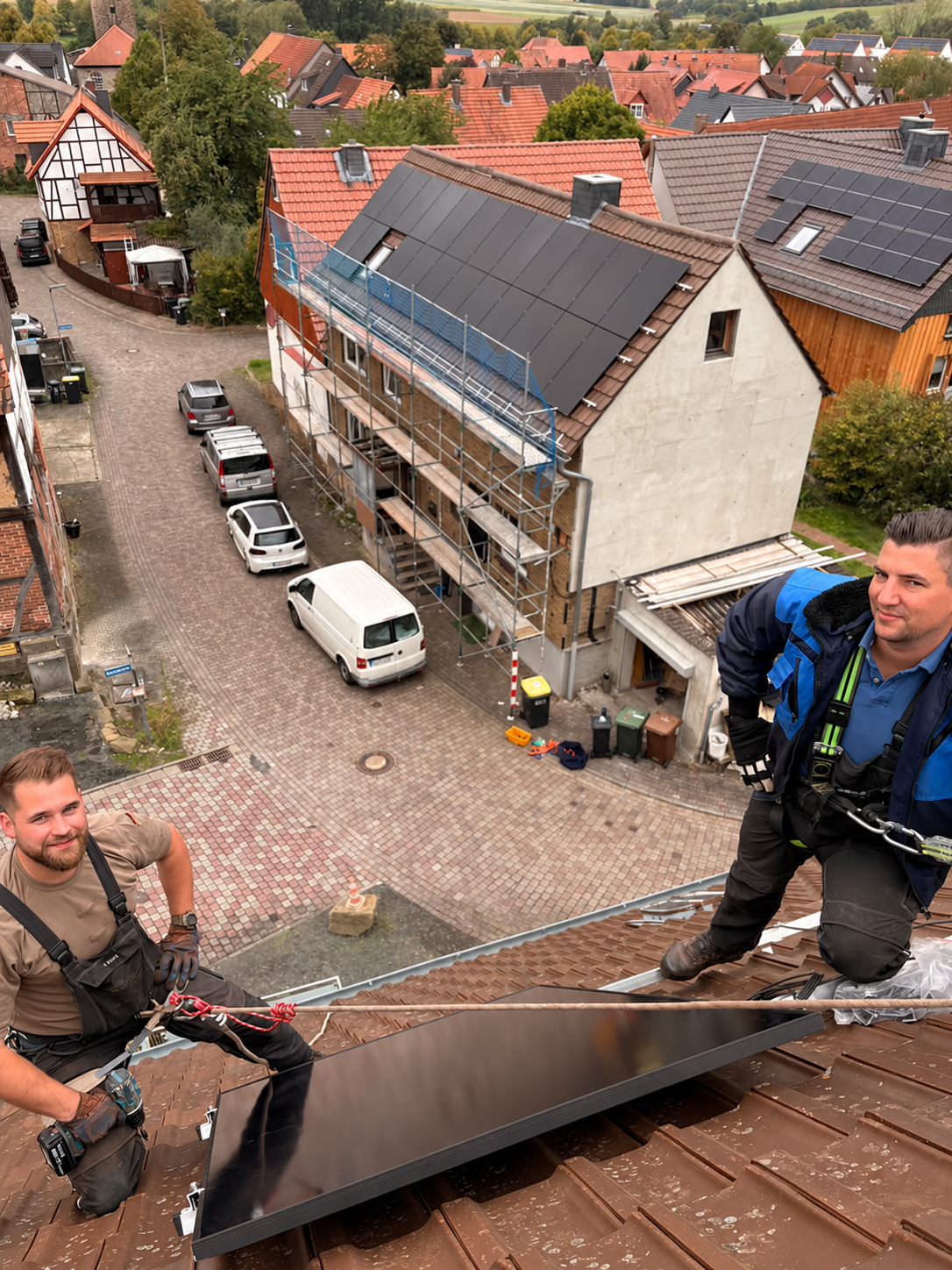 Zwei gesicherte Installateure mit einem Solarmodul auf einem Ziegeldach